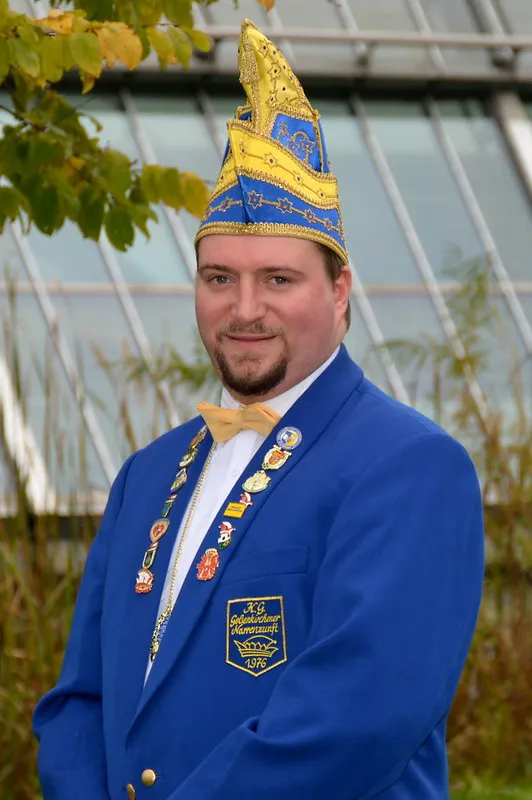 Porträt von Jens Kollatschni im blauen Sitzungsjackett mit Narrenkappe